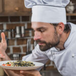 Séf egy étel felett koncentrál a konyhában, fókuszált munka egy mozgalmas környezetben.