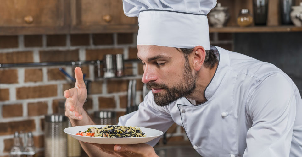 Séf egy étel felett koncentrál a konyhában, fókuszált munka egy mozgalmas környezetben.