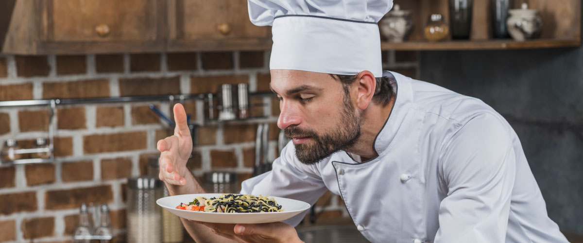 Séf egy étel felett koncentrál a konyhában, fókuszált munka egy mozgalmas környezetben.